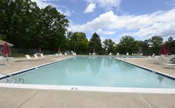 A swimming pool with chaise lounge chairs and trees in the background